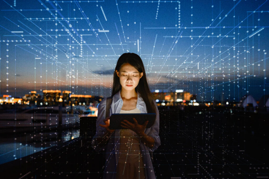 Woman using a tablet with a glowing digital UI overlay against a city skyline.
